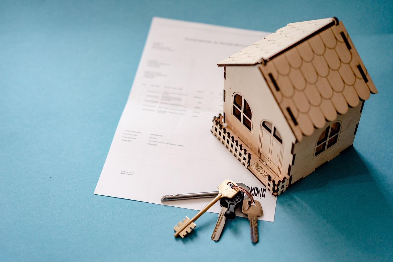 A model house sitting atop financial papers with house keys beside it.