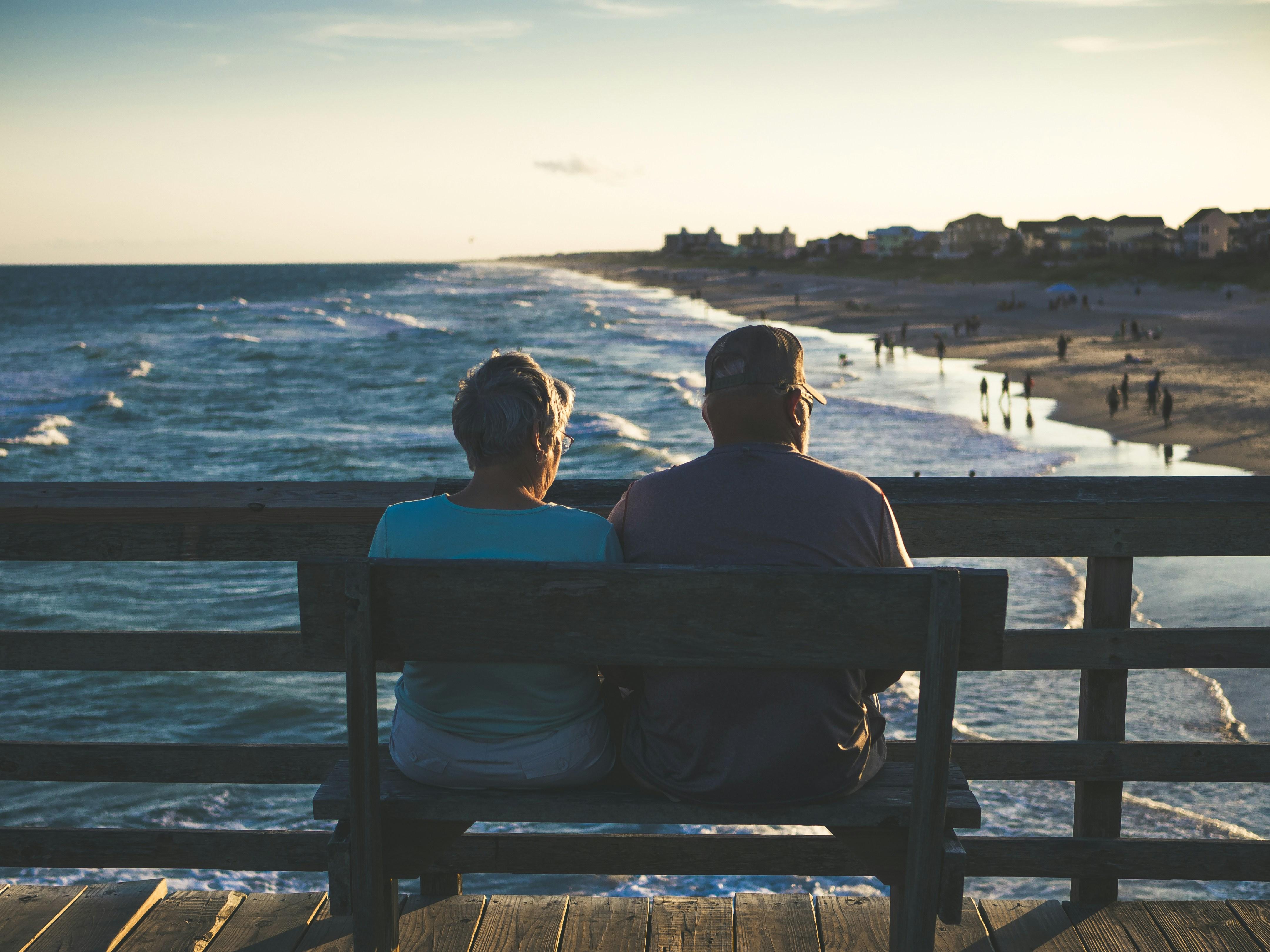 Old couple sitting on a bench looking at the ocean.